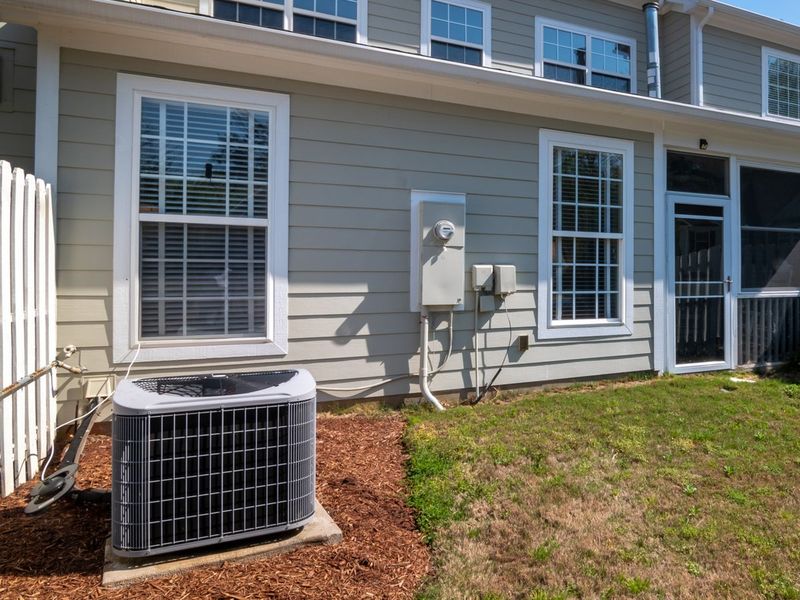 Outdoor air conditioner on a concrete pad beside a two-story house with gray siding