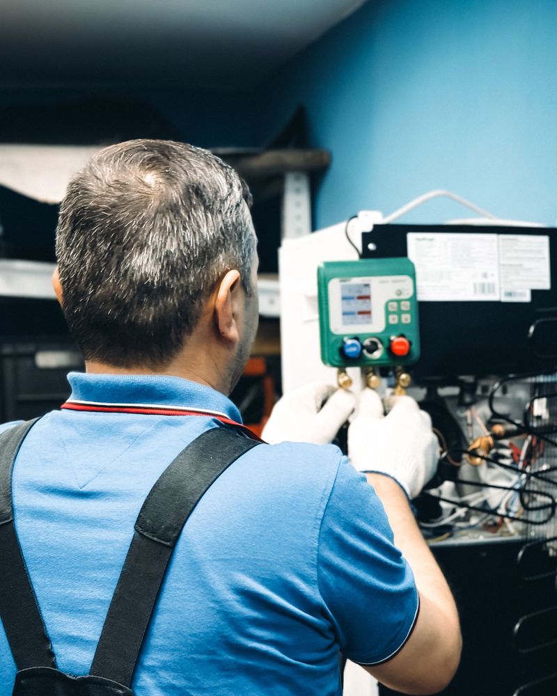 Technician in work gloves connecting refrigerant gauges to a cooling unit